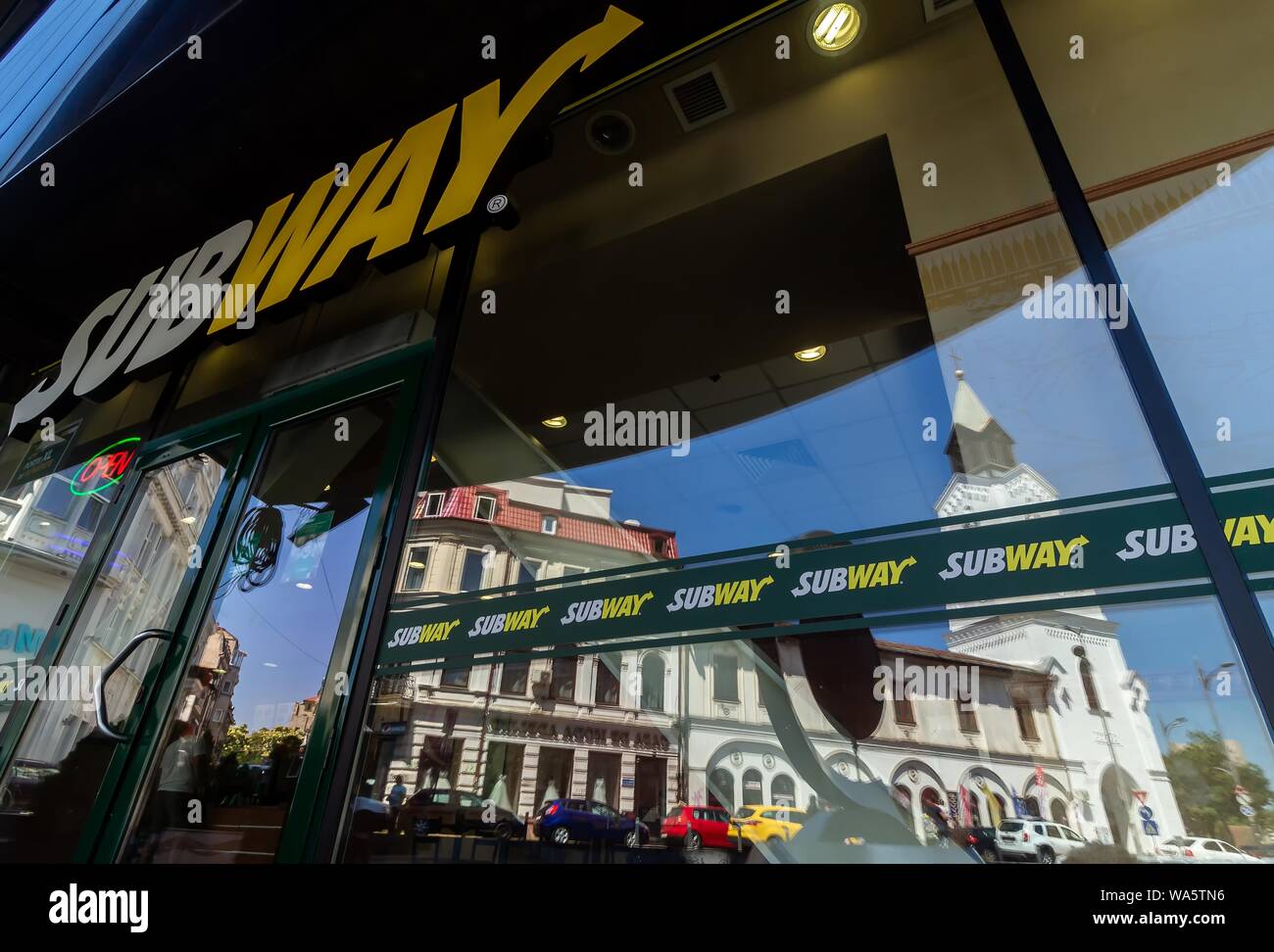 Bucharest, Romania - August 13, 2019: The Roman Catholic church 'Baratia', is seen in the reflection of the windows of a Subway fast food restaurant i Stock Photo
