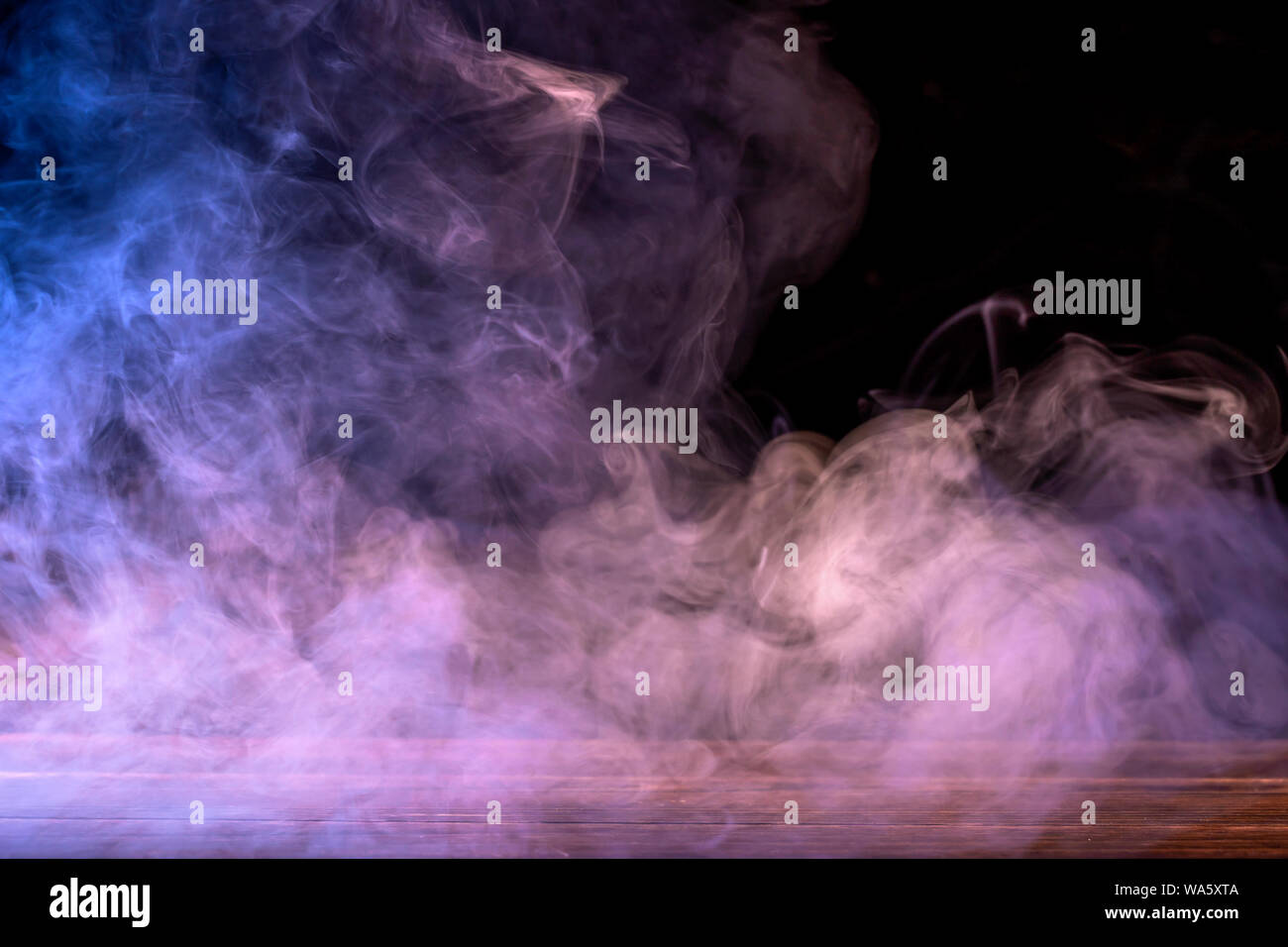 Conceptual image of multi-colored smoke isolated on dark black background and wooden table. Stock Photo
