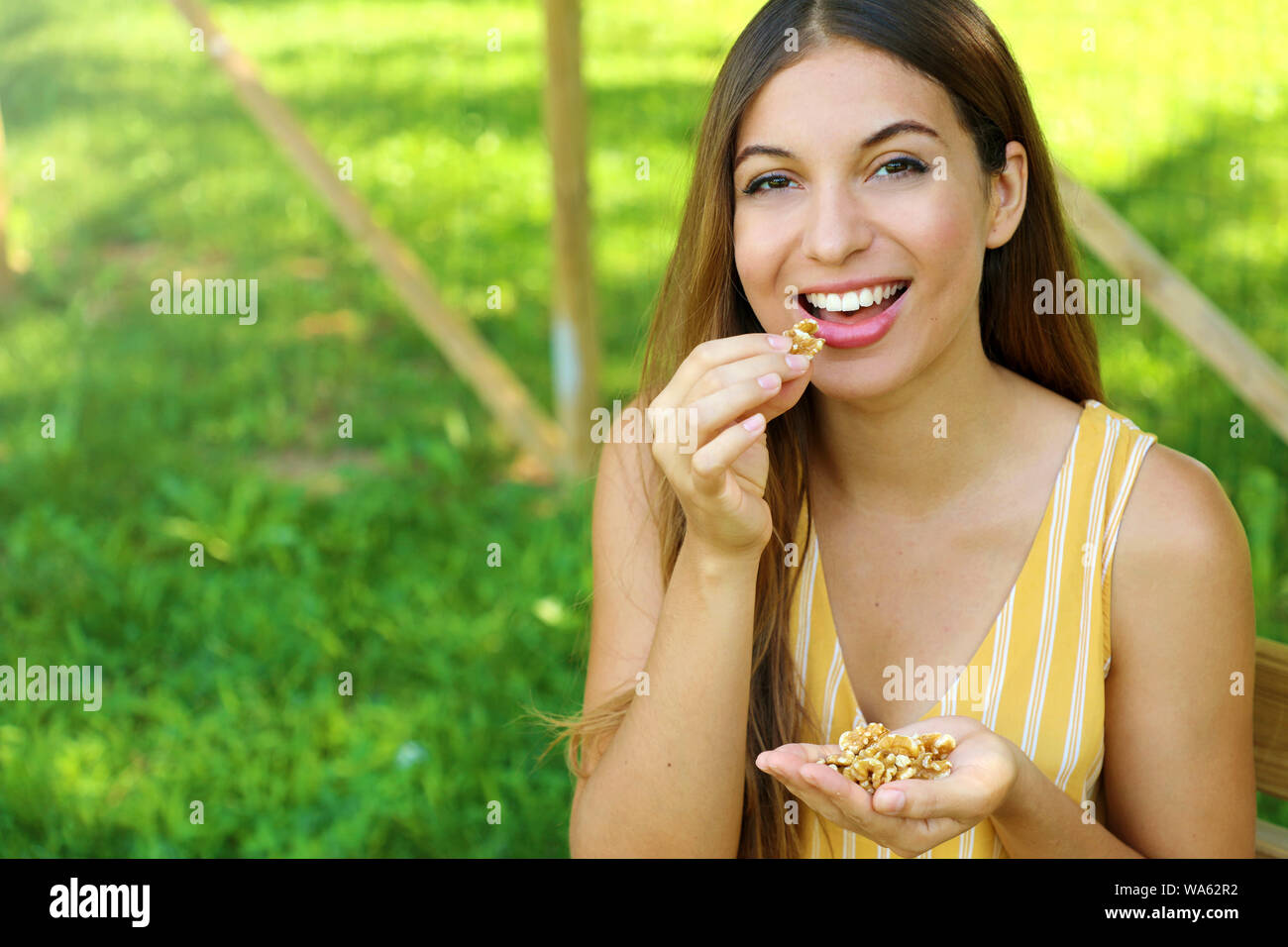 Beautiful smiling woman eating walnuts in the park. Healthy food