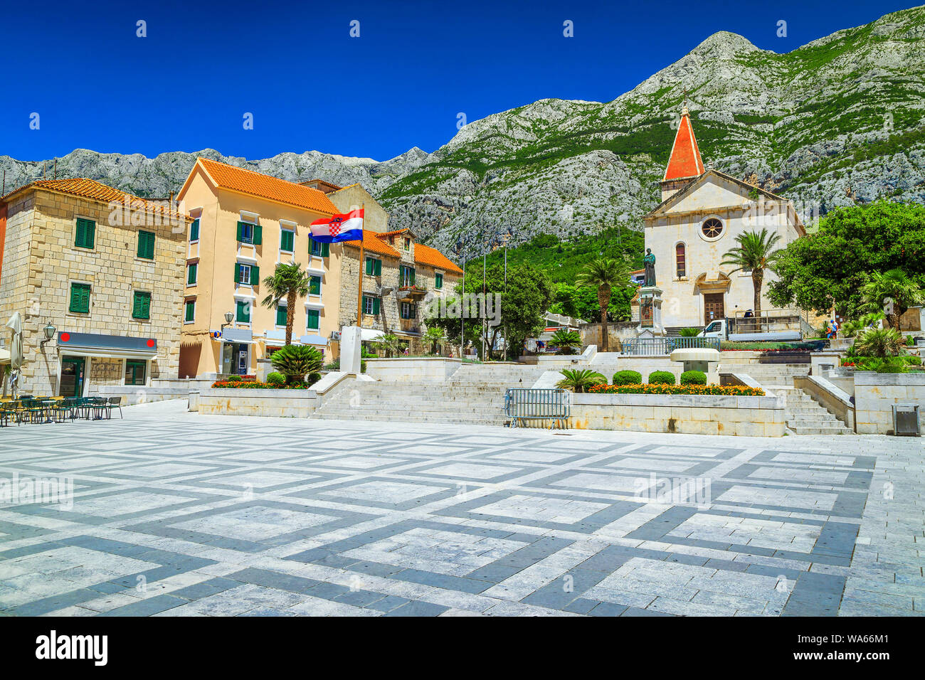 Popular mediterranean resort with beautiful old city center. Street cafees and catholic christian church in town square. High Biokovo mountains in bac Stock Photo