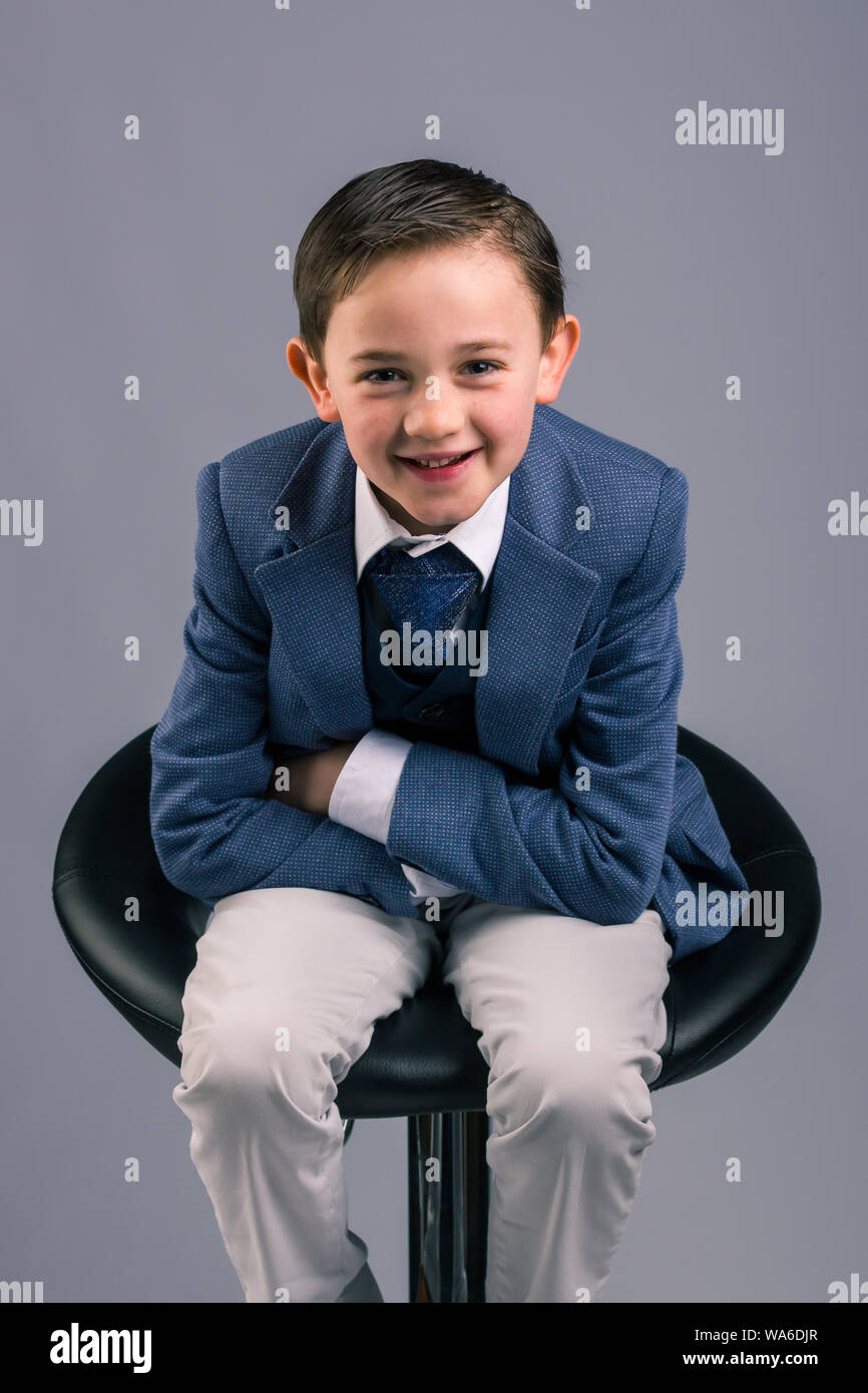 Portrait of 8 year old boy dressed in suit sitting on a stool with his