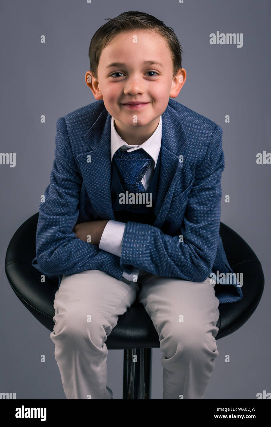 Portrait of 8 year old boy dressed in suit sitting on a stool with his