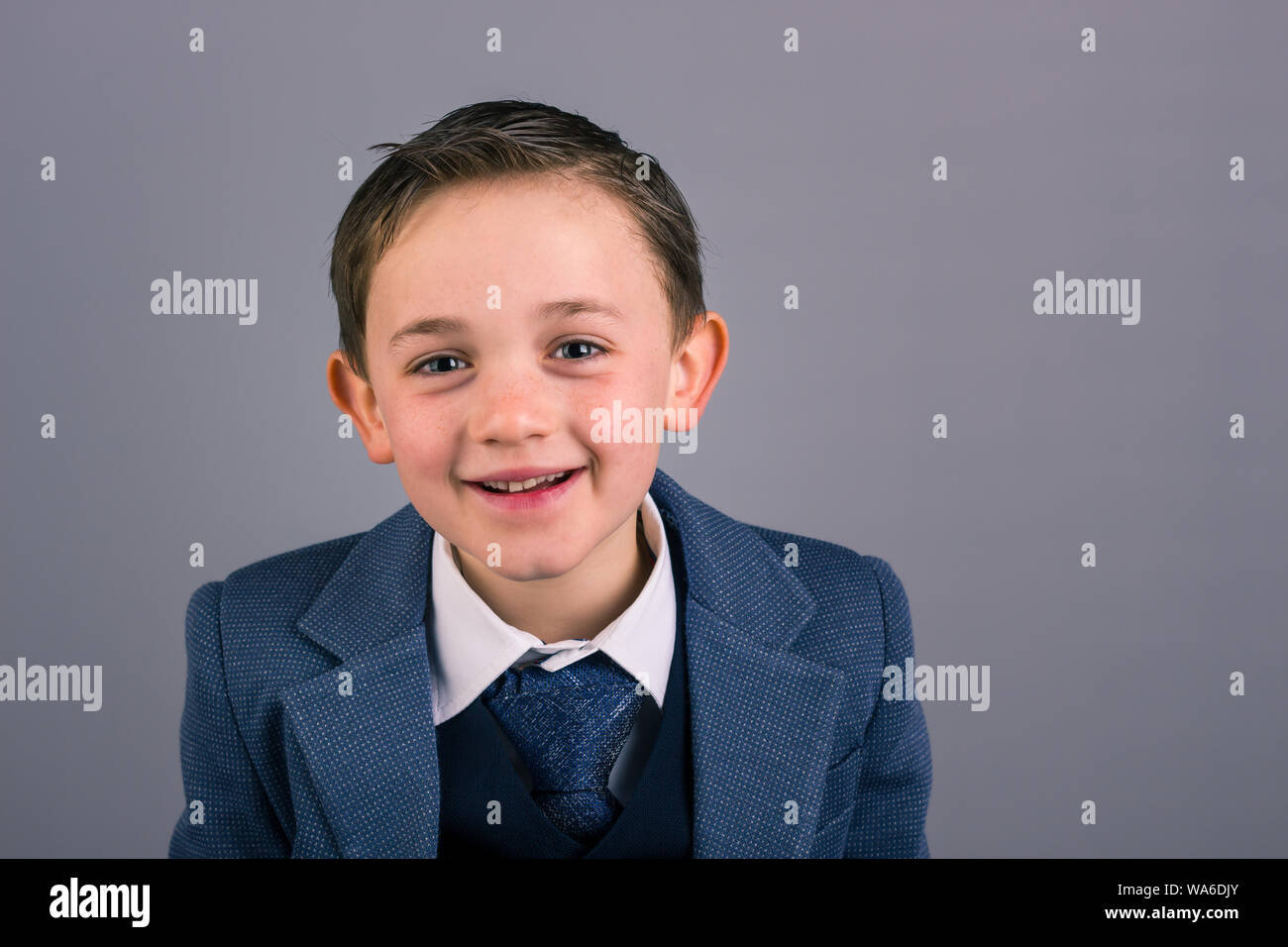 Portrait of 8 year old boy dressed in suit smiling isolated on gray