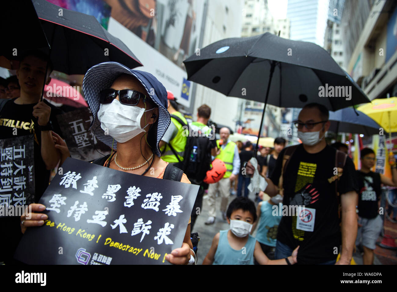 Hong Kong, China. 18th August 2019. A woman walks with a mask and a sign 'Free Hong Kong! Democracy Now!' through a shopping street to a protest rally in Victoria Park. Photo: Gregor Fischer/dpa Credit: dpa picture alliance/Alamy Live News Stock Photo