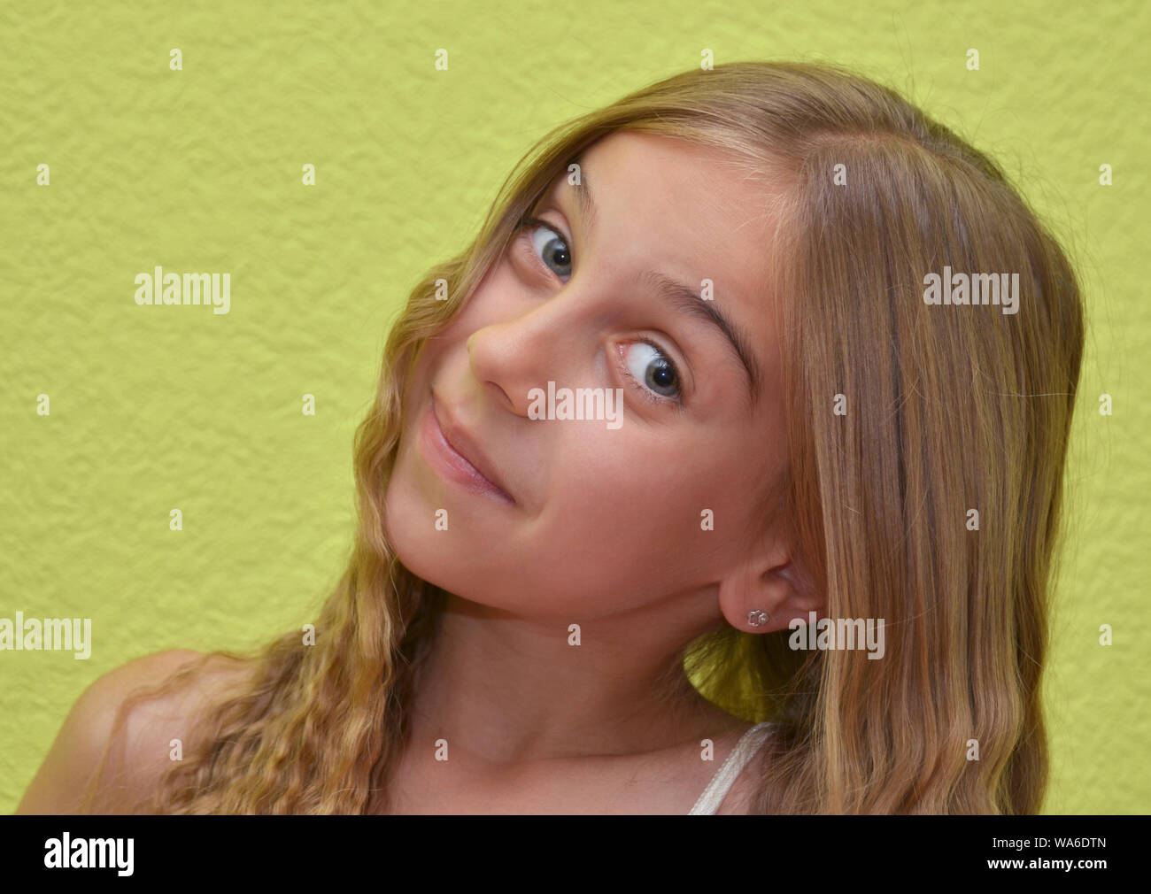 young blonde girl smiling into camera with light green background Stock Photo