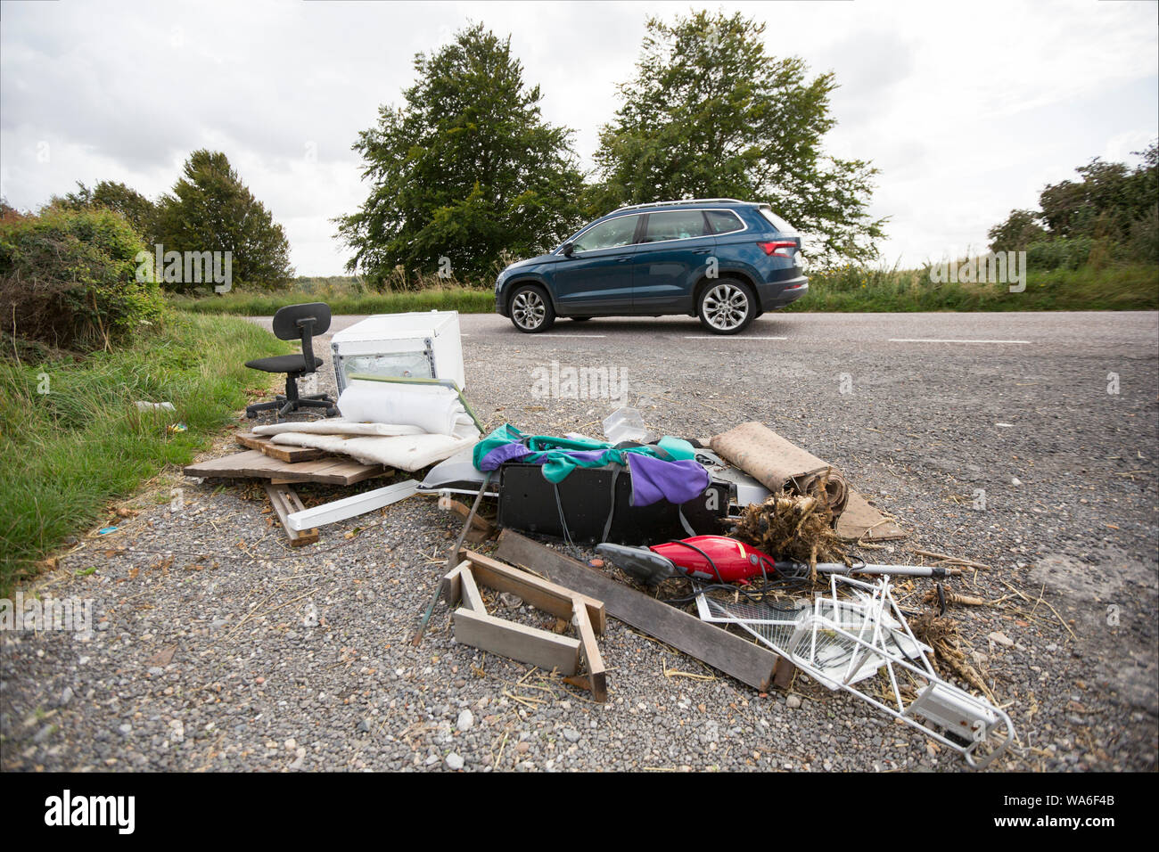 A vehicle passing rubbish dumped next to a country road in Dorset. Items include a flat screen television, a chair and rucksack. Dorset England UK GB Stock Photo