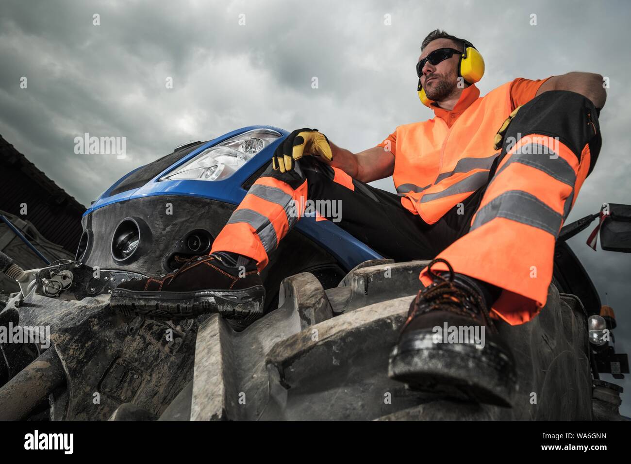 Road Construction Machine Operator Contractor. Industrial Job. Caucasian Worker Wearing Noise Protection Headphones Preparing For a Job. Stock Photo