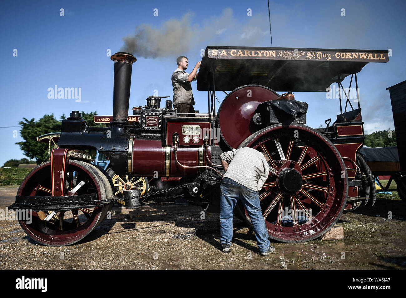 Men clean and polish their traction engine as it steams up at Drusilla's Inn, near Horton, Dorset, as dozens of steam powered vehicles prepare to make the journey to the Great Dorset Steam Fair, where they will be joined by thousands of enthusiasts celebrating steam power from August 22nd over the bank holiday weekend. Stock Photo
