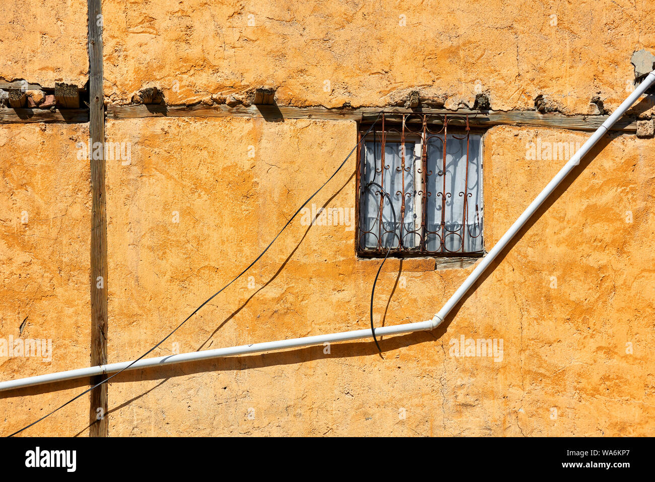 Vintage window with wrought iron grate and a pvc water pipe on old weathered facade of a house Stock Photo