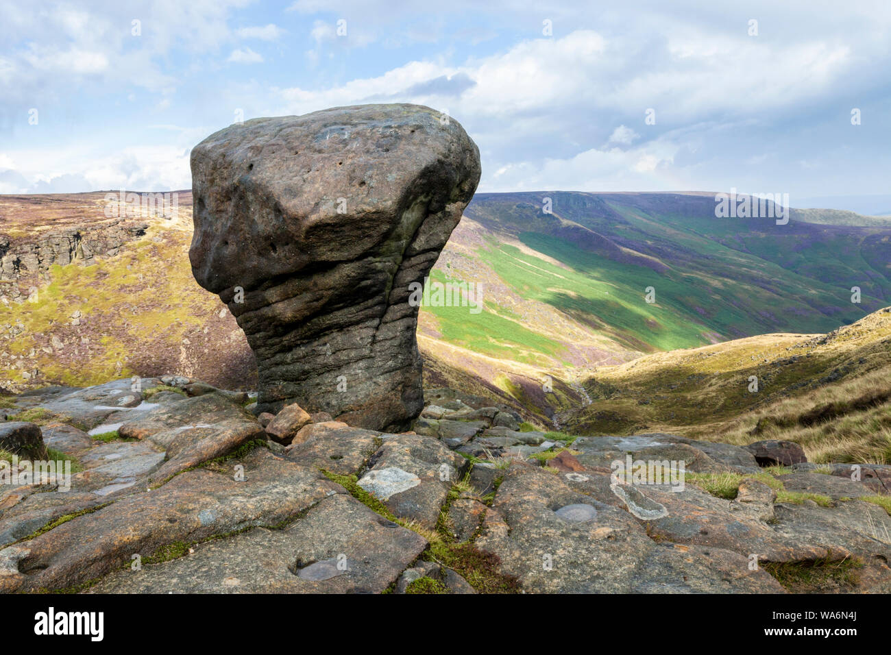 An eroded gritstone boulder and a view along Grindsbrook Clough and part of the southern edge of Kinder Scout, Derbyshire, Peak District, England, UK Stock Photo