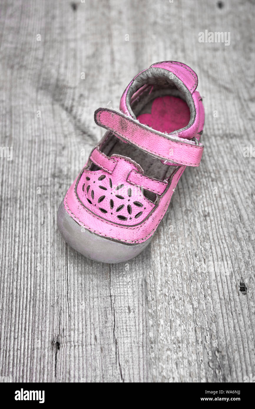 Worn pink children shoe on wooden plank background. Concept of child abuse or kidnapping or pedophilia. Stock Photo