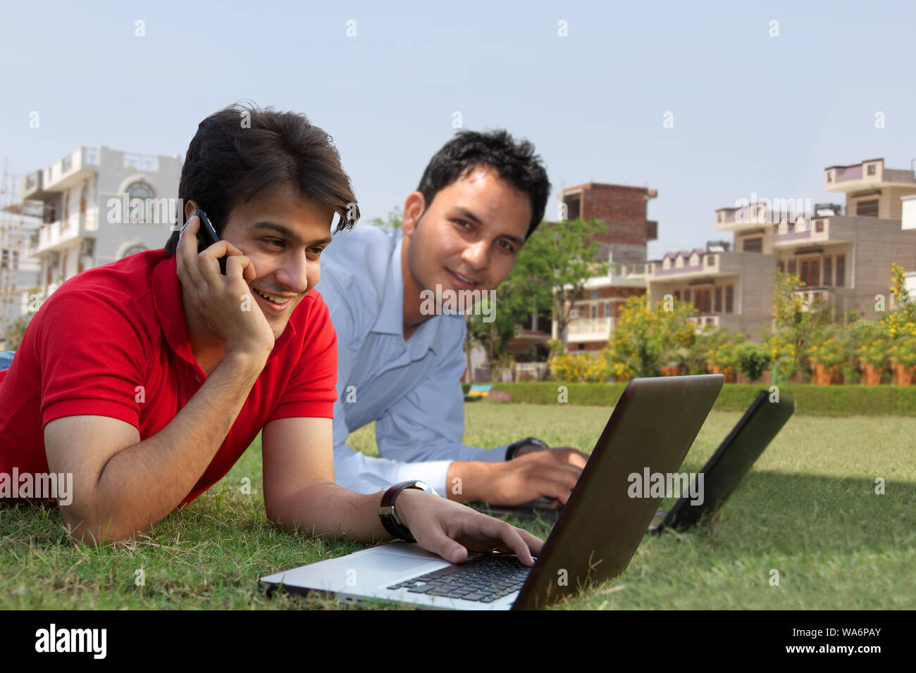 Young men lying on grass in lawn and using laptops Stock Photo