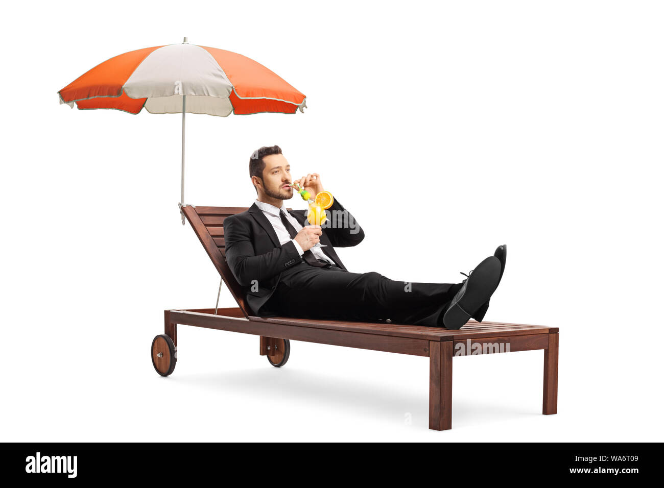 Young businessman in a suit lying on a sunbed under umbrella and sipping a cocktail isolated on white background Stock Photo