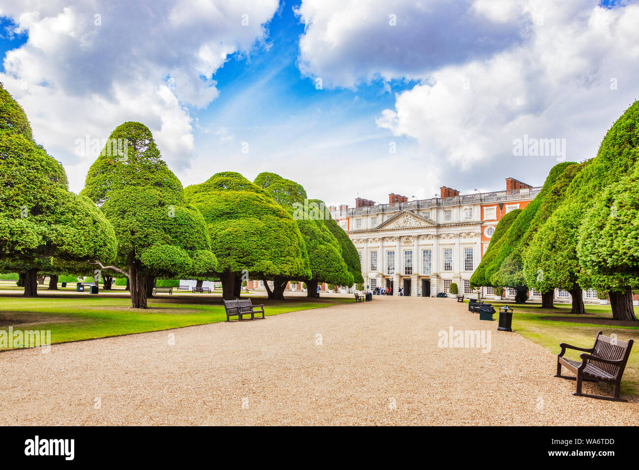 9 June 2019: Hampton Court, Richmond UK - The East Front of the palace, seen beyond an avenue of yew trees in the Great Fountain Garden, with a group Stock Photo