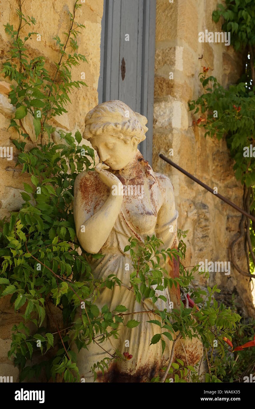 A stone statue of a lady with greenery growing around it Stock Photo