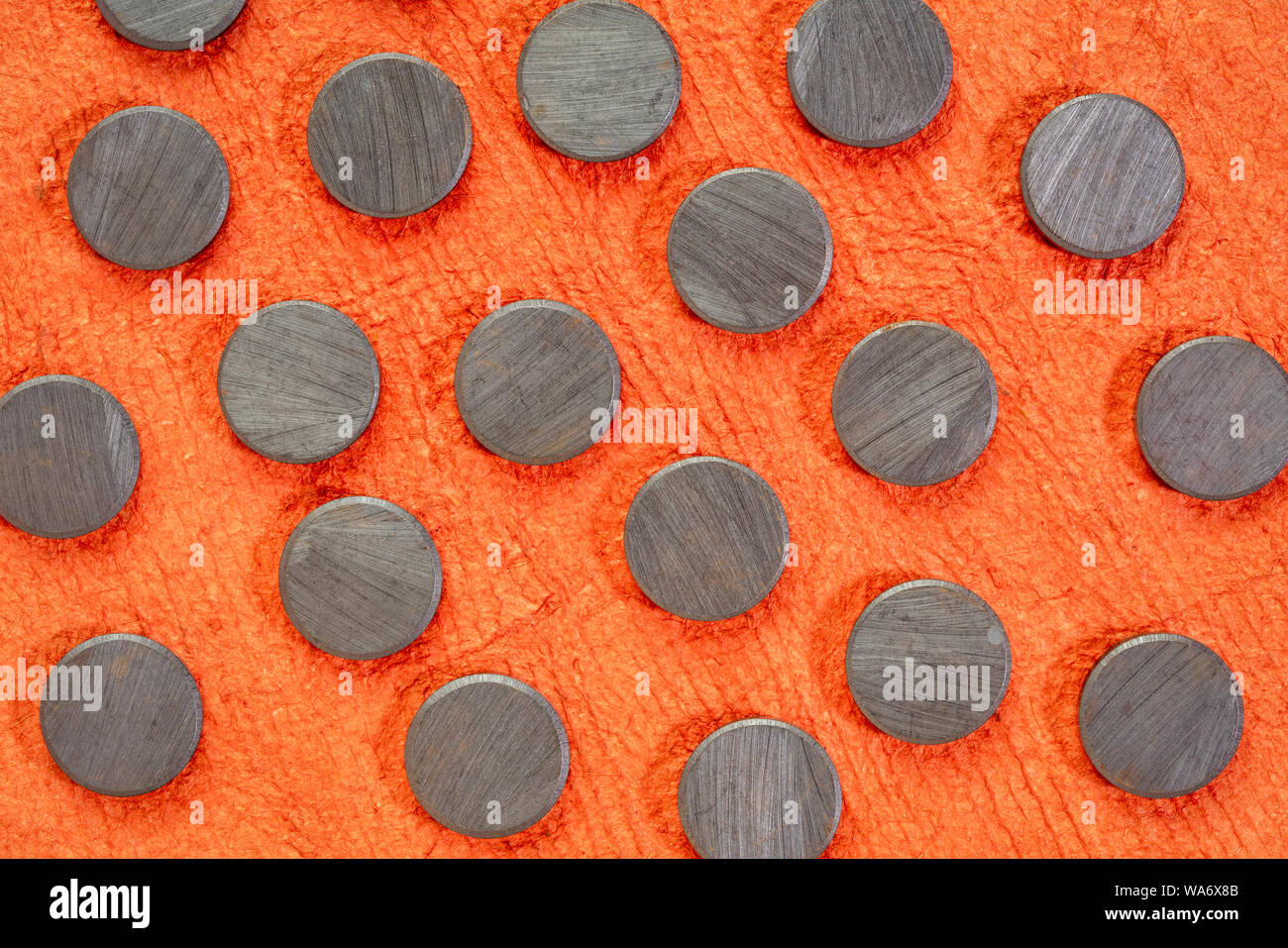 set of small round ceramic ferrite magnets - top view against textured orange bark paper Stock Photo