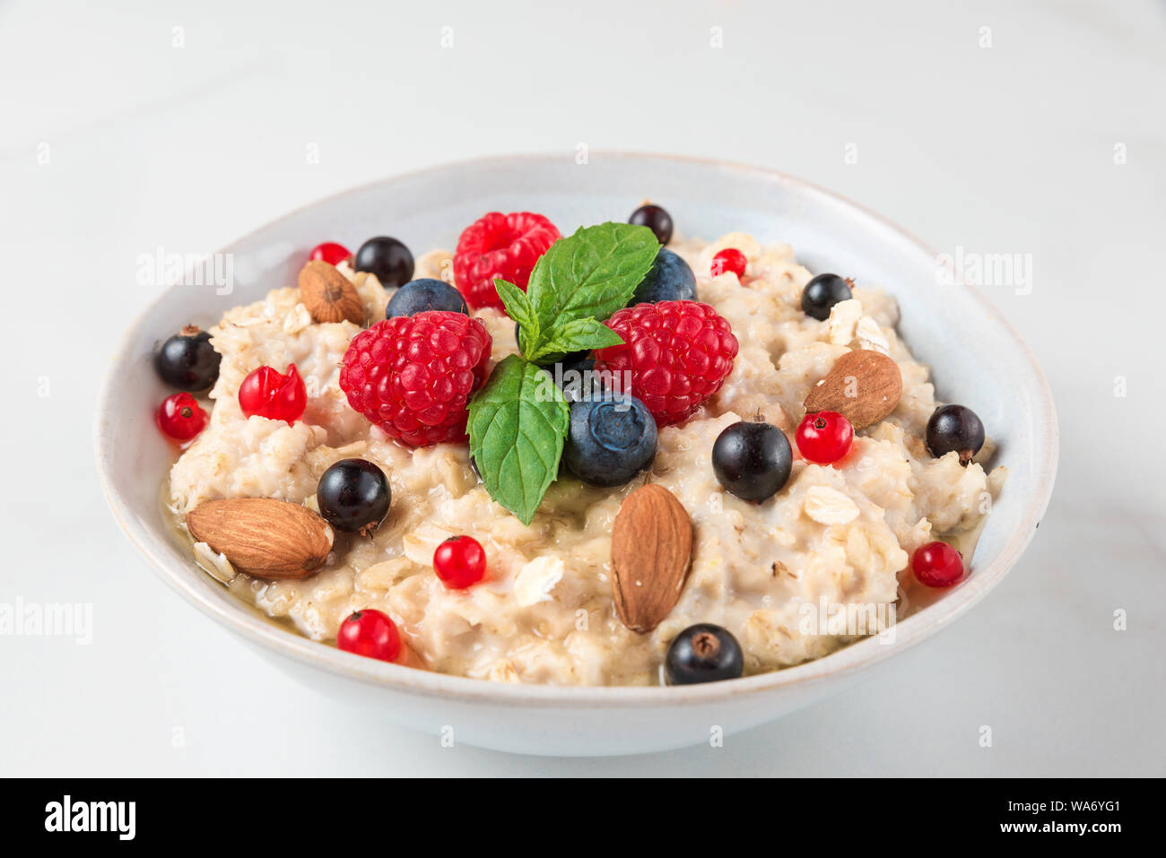 oatmeal porridge with fresh berries, nuts, honey, mint in a bowl for healthy diet breakfast. close up Stock Photo