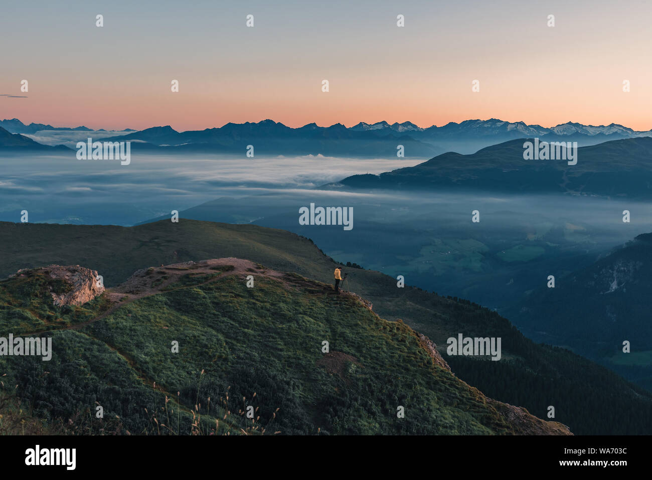 Nature photographer in action. Man standing on the mountain above a misty clouds waiting for sunrise. morning mountain landscape Stock Photo