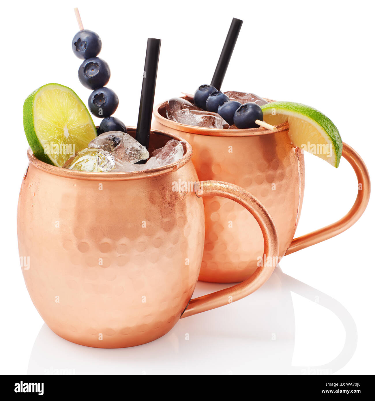 Icy cold Moscow mule cocktail with ginger beer, vodka, lime and blueberries in copper mugs with reflection isolated on white background Stock Photo