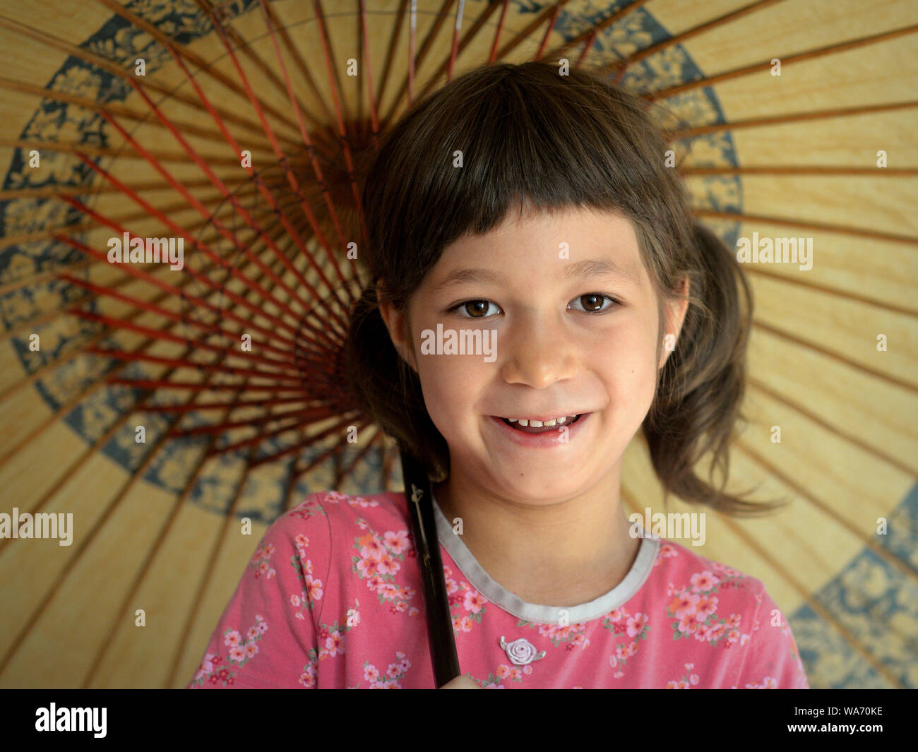 Cute mixed-race little girl (Caucasian and Southeast Asian) smiles under her traditional Chinese oil-paper parasol. Stock Photo