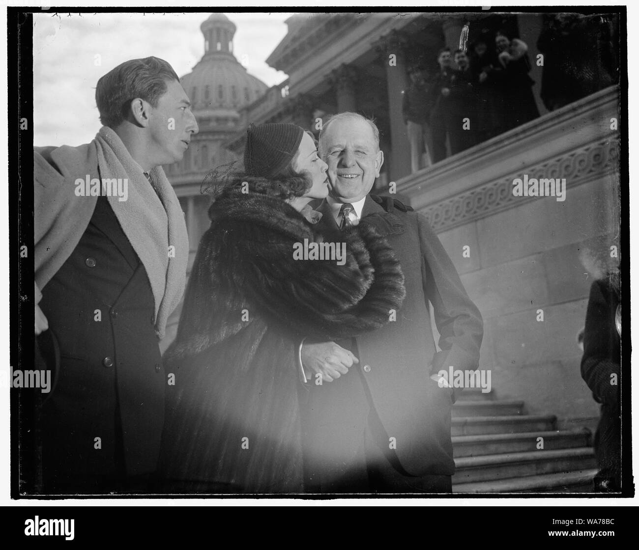 A movie kiss planted on Maryland Senator. Washington, D.C., Jan. 27. Following a reception by the Senators at the Capitol today, Eleanor Powell, movie and screen star, plants a daughterly goodbye kiss on the cheek of Senator George L. Radcliffe of Maryland. On the left is Ray Bolger, another dancing star, who with miss Powell will entertain patrons of the many presidents' birthday parties in Washington this Saturday, 1/27/38 Stock Photo