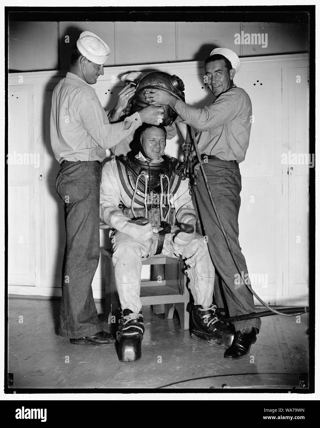 Add record depth reached by Navy divers. William Badders, Master Diver, U.S.N., who recently made a record dive of over 500 feet, is helped into his underwater suit just before taking an experimental dive in the tank at Washington Navy Yard, 8/9/38 Stock Photo