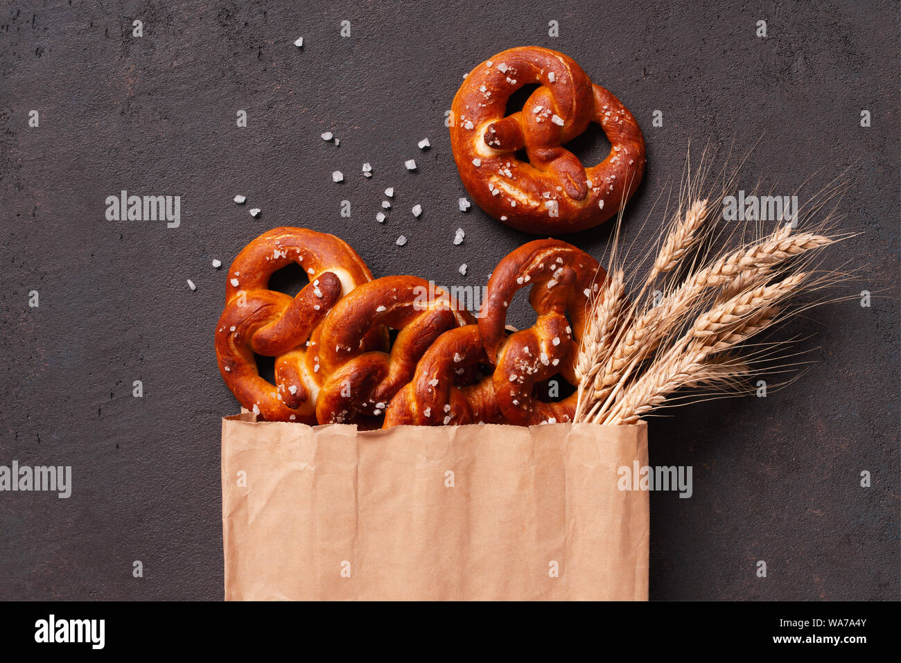 Fresh salted pretzels in the paper bag on the brown table decorated with wheat ears, top view composition Stock Photo