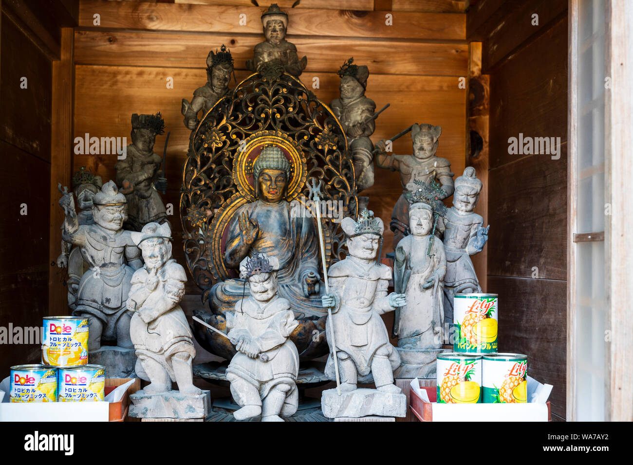 Japan, Miyajima. Daisho-in temple, the Yakushi Nyorai Buddha with guardians in front and offerings of tinned pineapple at the Yakushi-do Hall. Stock Photo