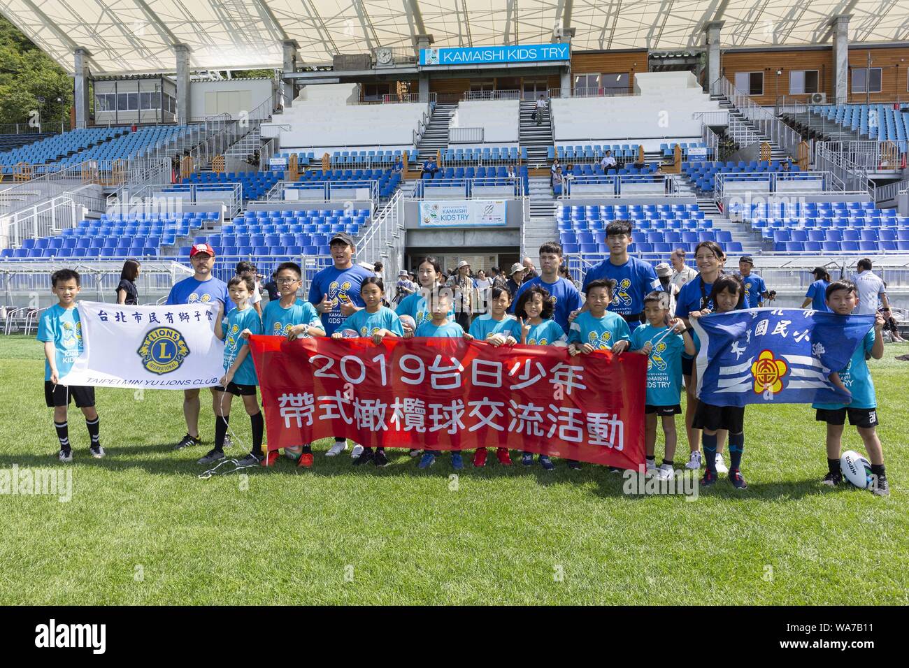 Kamaishi, Japan. 18 August 2019.  Elementary-school children from Taiwan and organizers of the ''Kamaishi Kids Try'' sports event pose for the cameras at Kamaishi Unosumai Memorial Stadium. The ''Tohoku Media Tour: Iwate Course'' is organized by the Tokyo Metropolitan Government in collaboration with local authorities to showcase the recovery efforts in Tohoku area affected by the 2011 Great East Japan Earthquake and Tsunami.  Th Credit: ZUMA Press, Inc./Alamy Live News Stock Photo