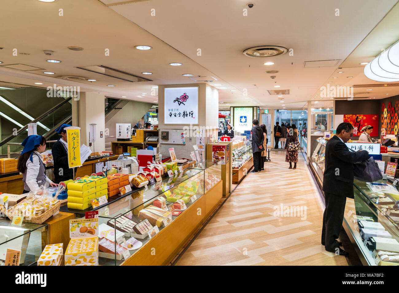 Japan, Hiroshima station interior. View along sweet gift counter and aisle to shopping area entrance. Salaryman at one counter, other people looking. Stock Photo