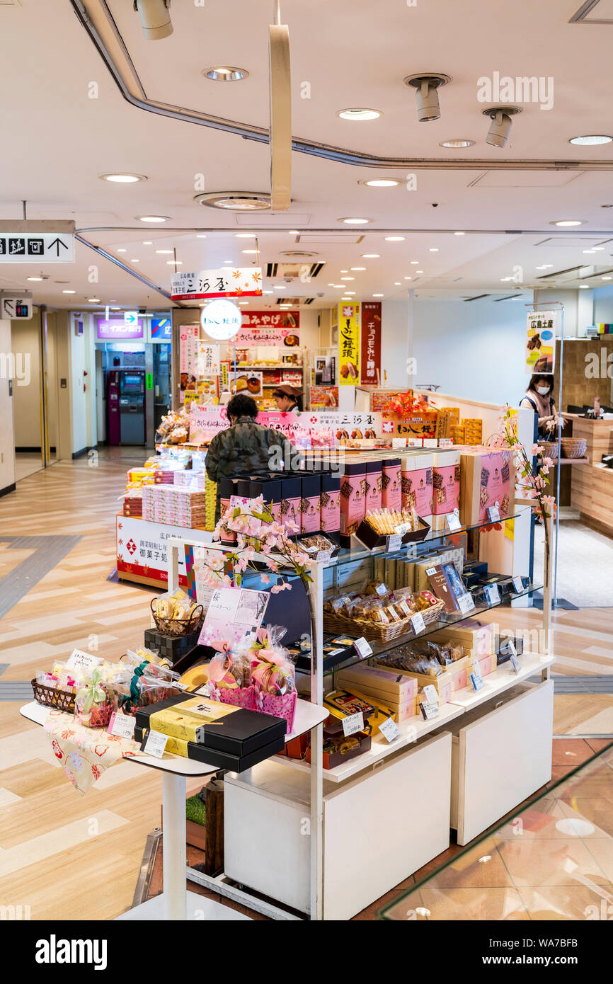 Japan, Hiroshima station interior. Brightly lit shopping area with Sweets and souvenirs stacked on on display stands on wooden floor. Stock Photo