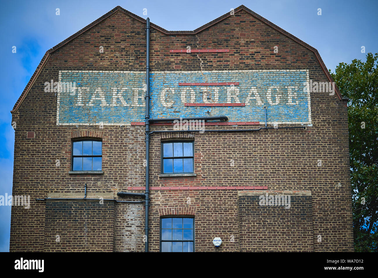 A blue and white 'ghost' sign saying 'take courage' on a brickwork facade of an old brewery in central London. Landscape format. Stock Photo