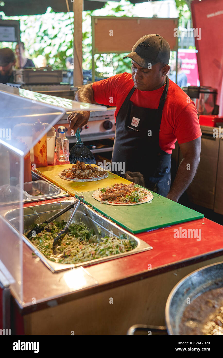 London, UK - August, 2019. A man preparing a chicken wrap in a Mexican street food stall in Borough Market. Stock Photo