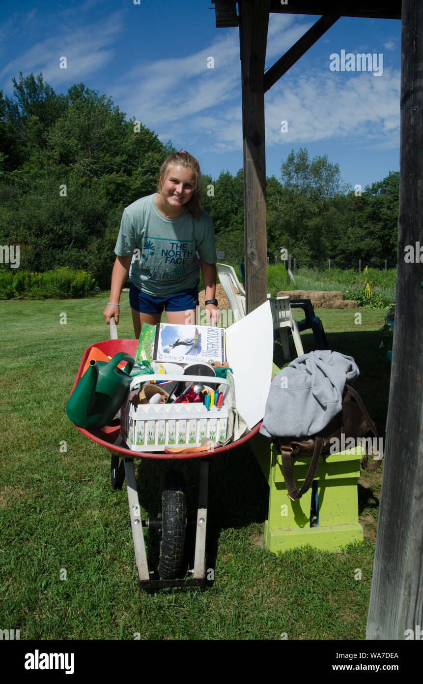 Young woman pushing wheelbarrow with equipment for childrens camp in Yarmouth Community Garden, Maine,, USA Stock Photo