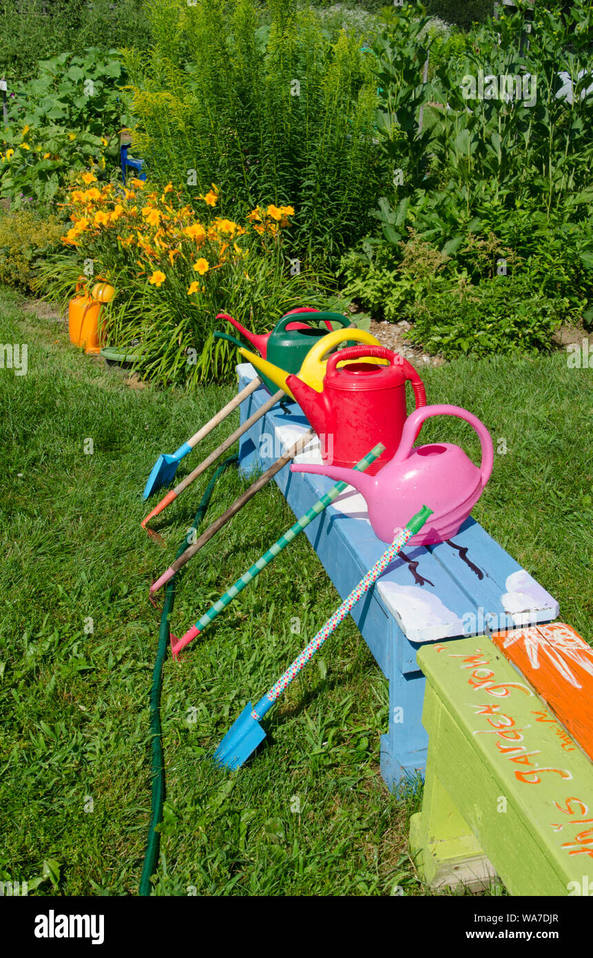 Colorful watering cans and toy shovels and tools lined up for community garden summer learning camp for kids, Yarmouth, Maine, USA Stock Photo