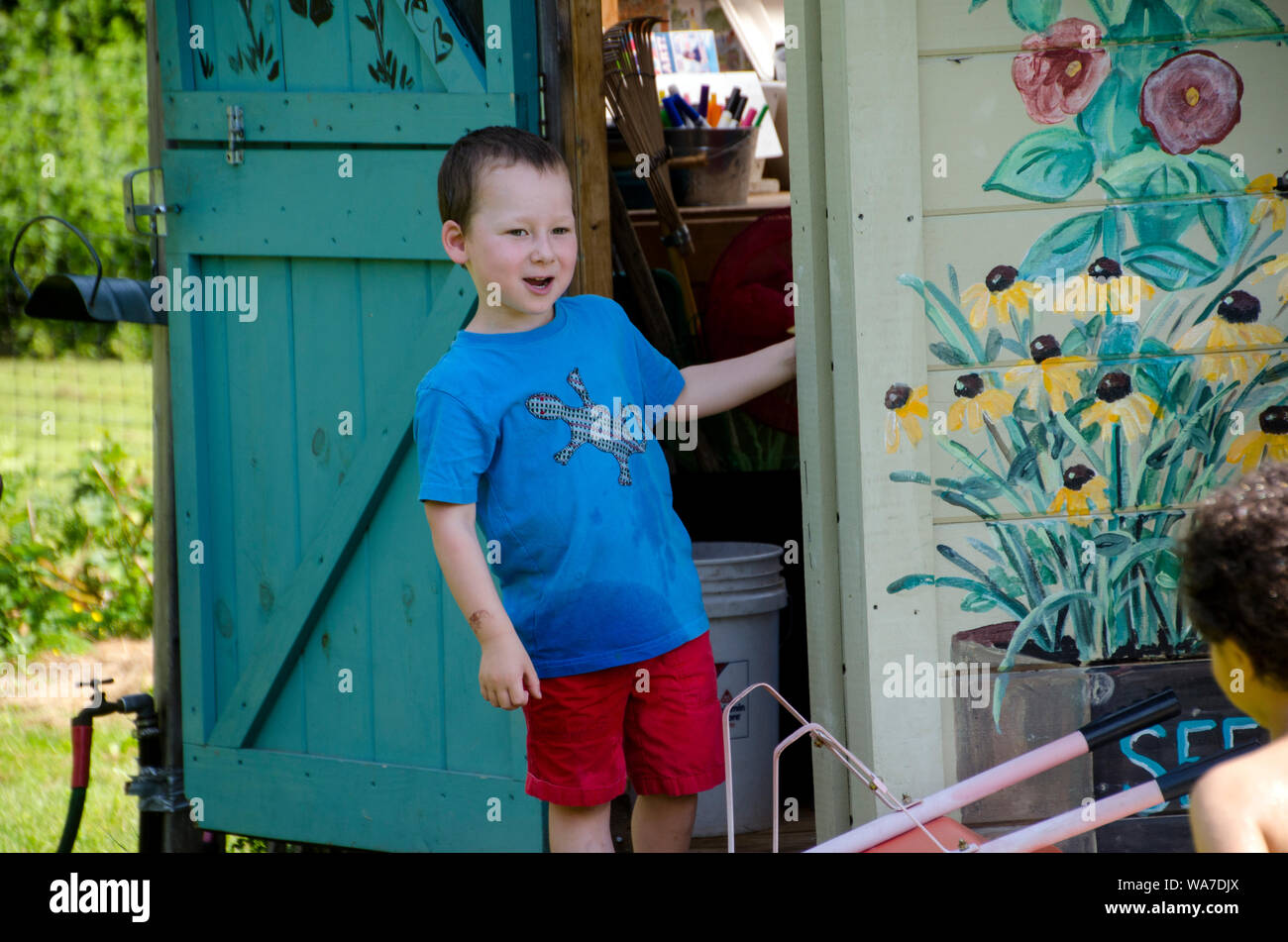 Boy standing beside shed in commmunity garden, Maine, USA Stock Photo