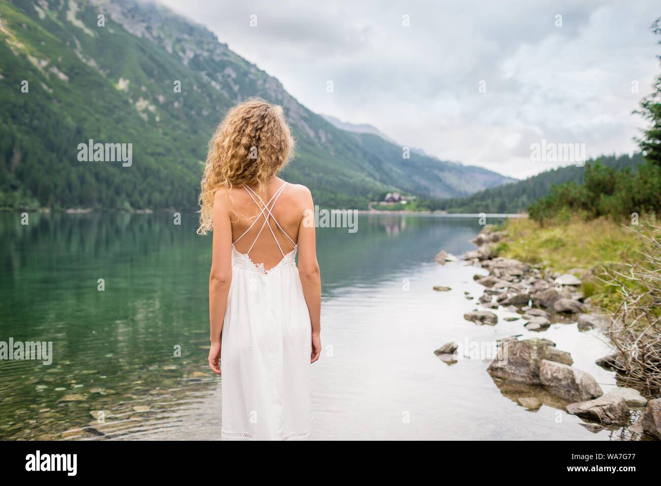 Beautiful Young Woman With Curly Hair In A White Dress Stands Near