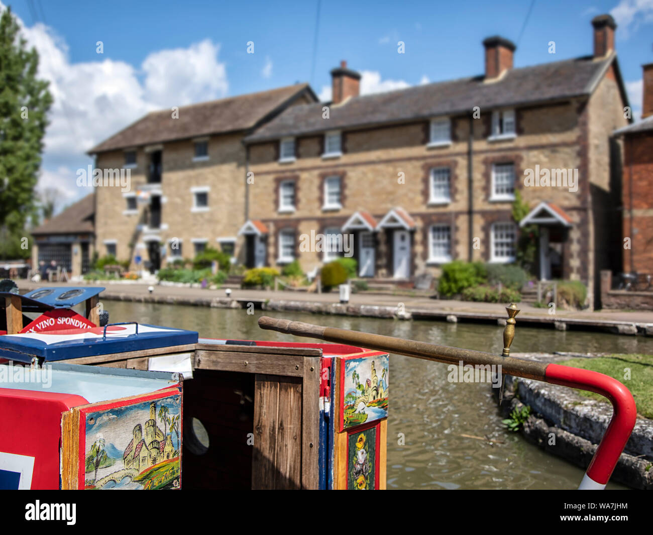 STOKE BRUERNE, NORTHAMPTONSHIRE, UK - MAY 10, 2019:  Pretty canalside cottages seen above colourful tiller and traditional painting on narrowboat Stock Photo