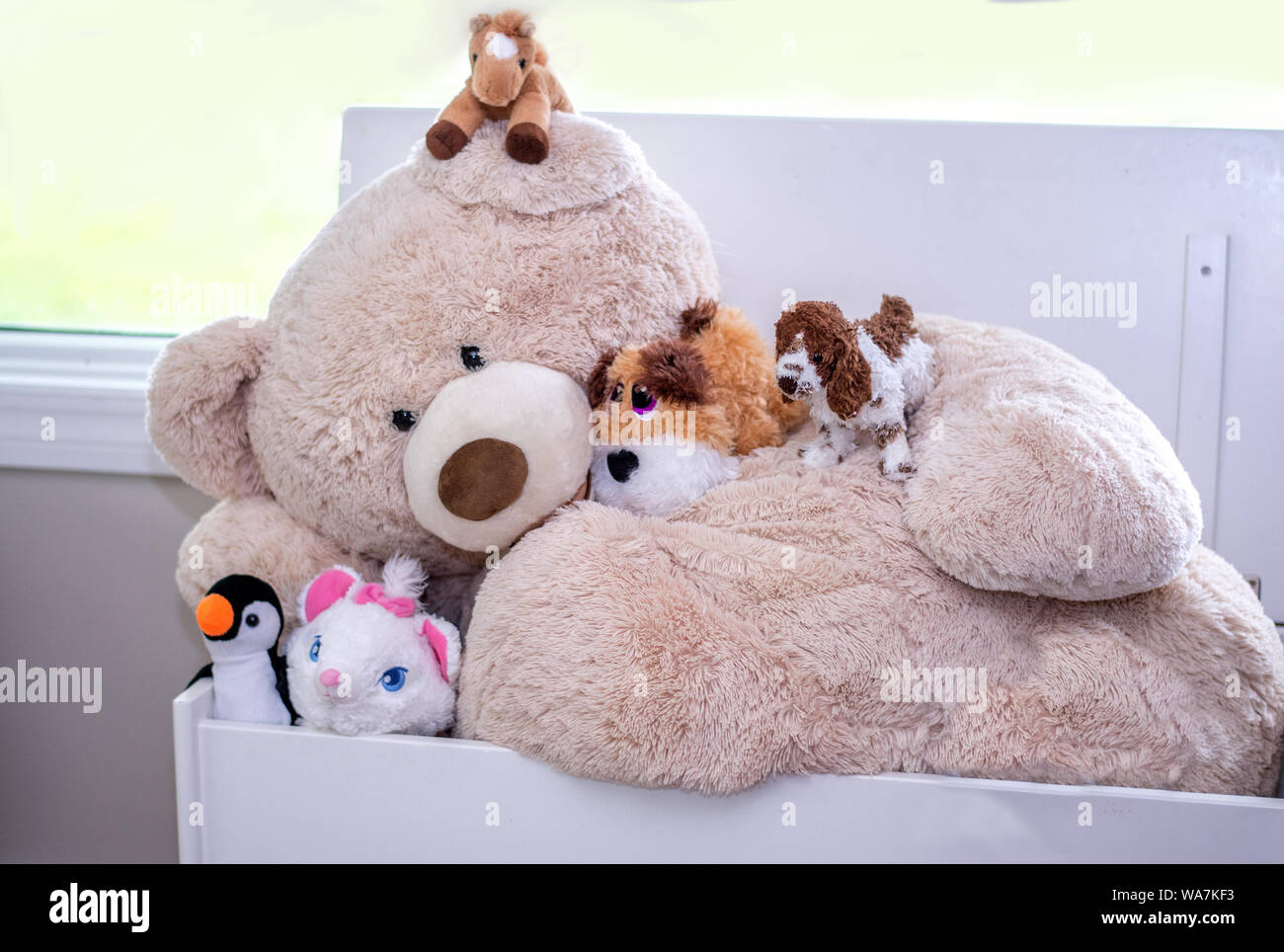 A large stuffed bear is covered with many smaller stuffed toys, a toy friendship in the playroom Stock Photo