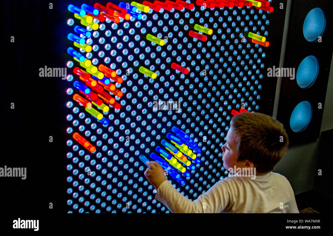 a young boy plays with colorful plastic pegs and a giant light bright screen, to create beautiful patterns at a children's museum Stock Photo