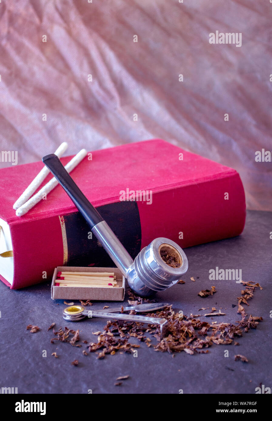 aristocob pipe with tobacco, resting against a red book with copy space  Stock Photo