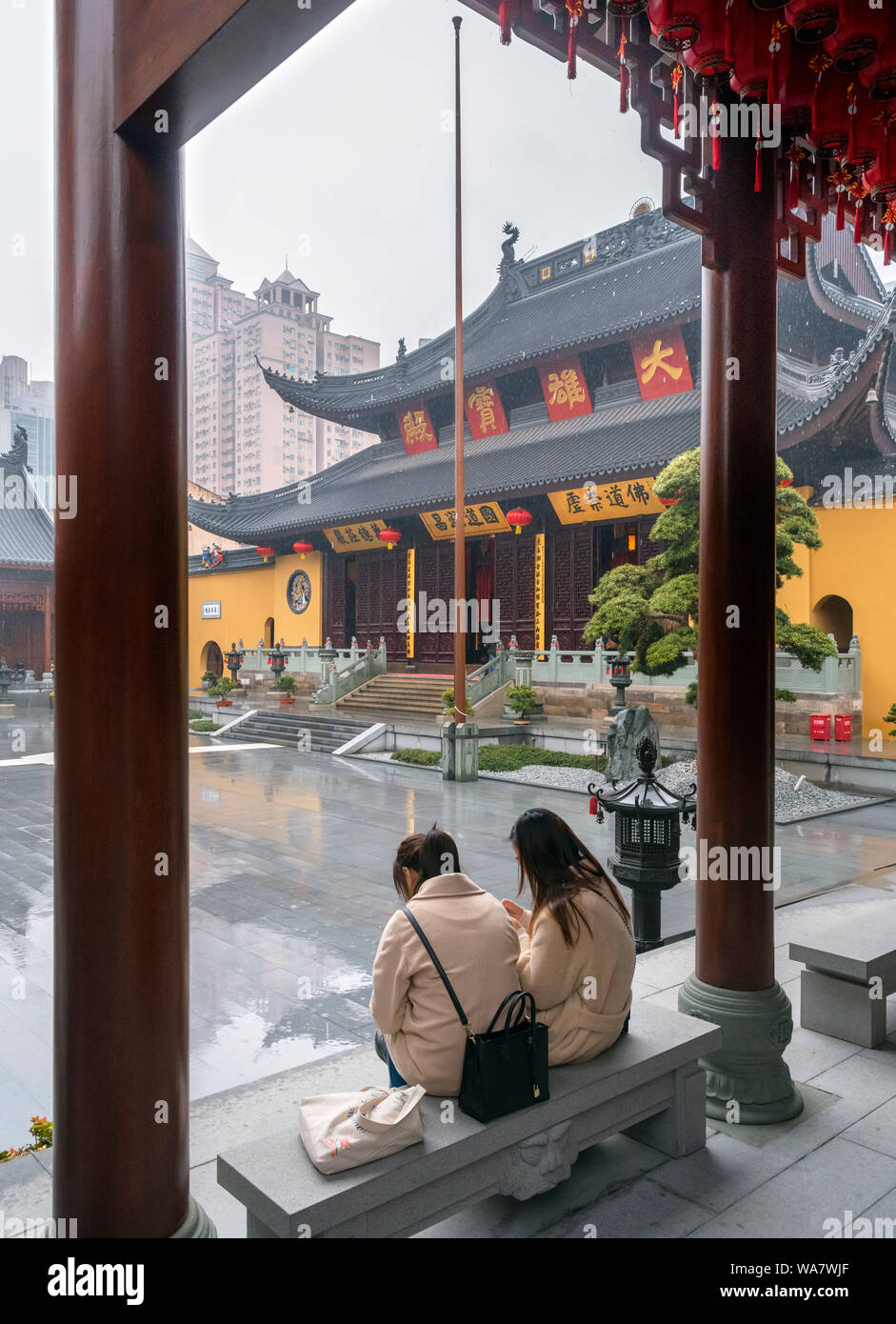 Two young women sheltering from the rain in front of the Grand Hall at the Jade Buddha Temple, Shanghai, China Stock Photo