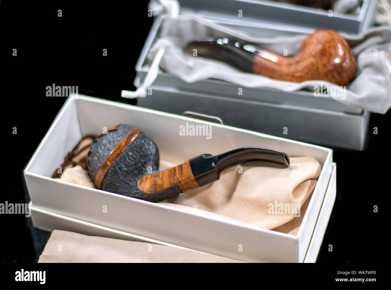 Beautiful smoking pipes in white gift boxes are display against a black