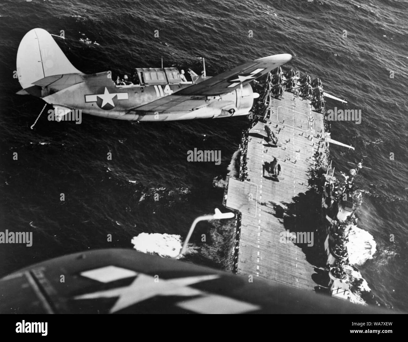 Curtiss SB2C Helldiver, a carrier-based dive bomber aircraft during World War 2. Curtiss SB2C-3 Helldiver aircraft banks over the USS Hornet (CV-12), aircraft carrier before landing, following strikes on Japanese shipping in the China Sea, circa 1945 Stock Photo