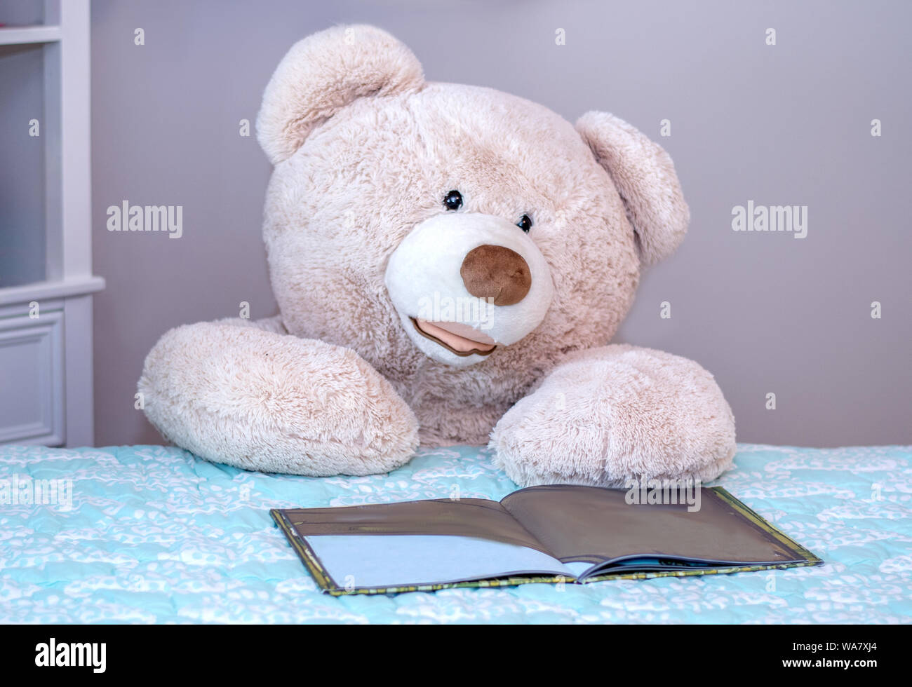 Big teddy bear kneels beside the bed and reads a child's picture book Stock Photo