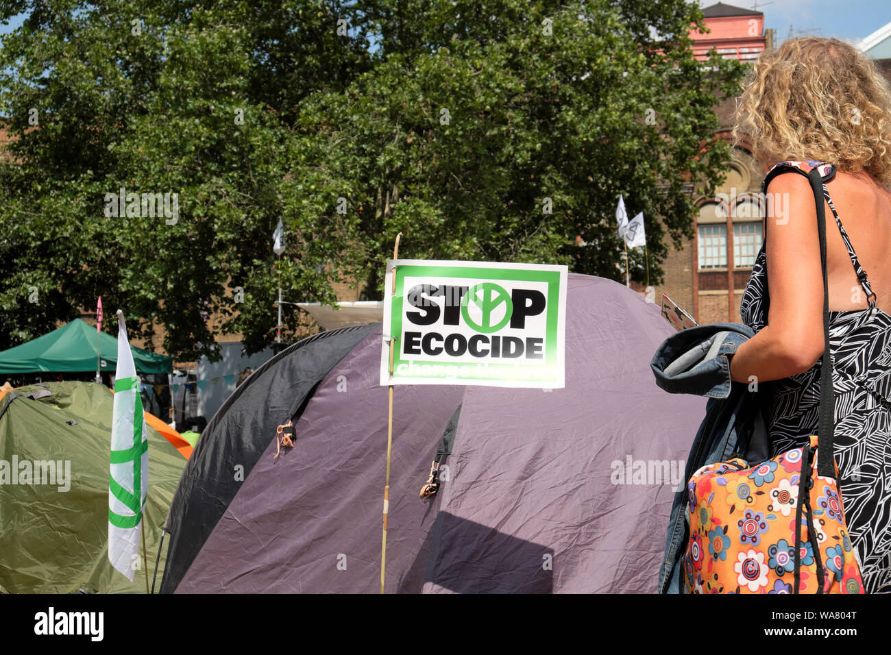 Stop Ecocide sign, woman and tents in the park Extinction Rebellion Waterloo Millennium Green in South London SE1  England UK  KATHY DEWITT Stock Photo