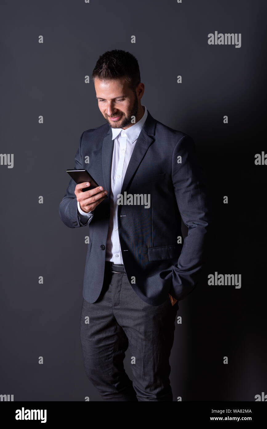 A smiling handsome young businessman in a suit using his smartphone in ...