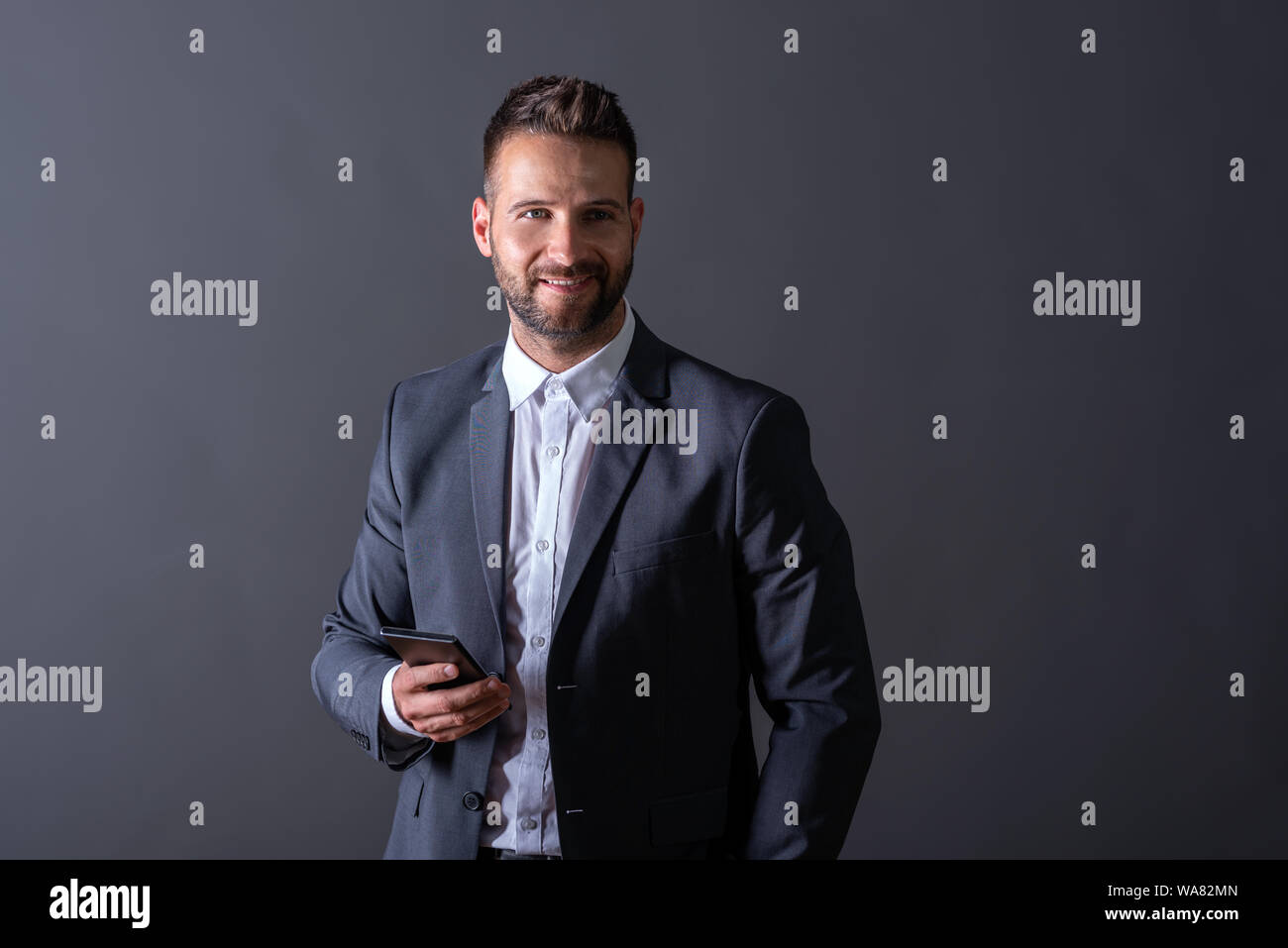 A smiling handsome young businessman in a suit using his smartphone in ...