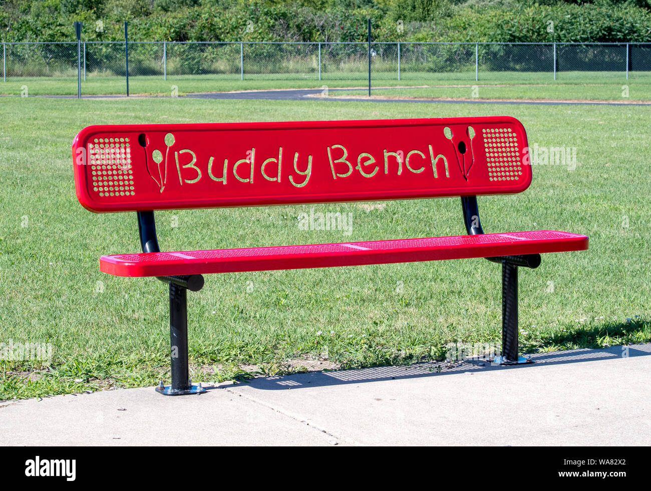 red buddy bench on a school play ground. A bench for a shy or lonely child to sit on to indicate they need a friend or a buddy Stock Photo