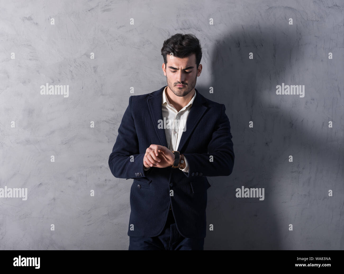 A serious handsome young businessman in a black suit checking the time ...